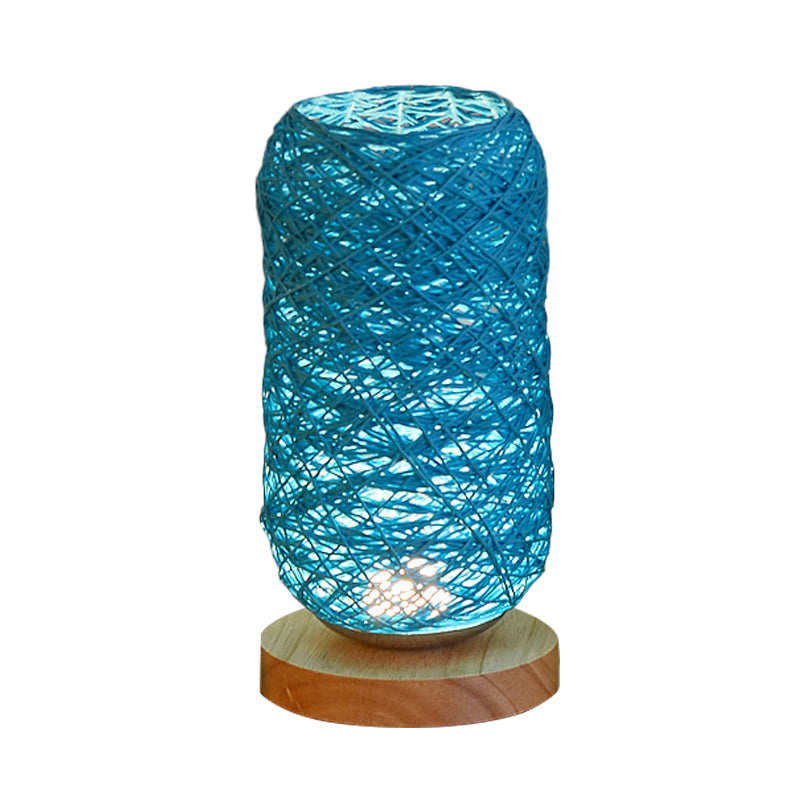 Geflochtene Tischlampe in Blau mit zylindrischer Form und Holzsockel vor hellem Hintergrund