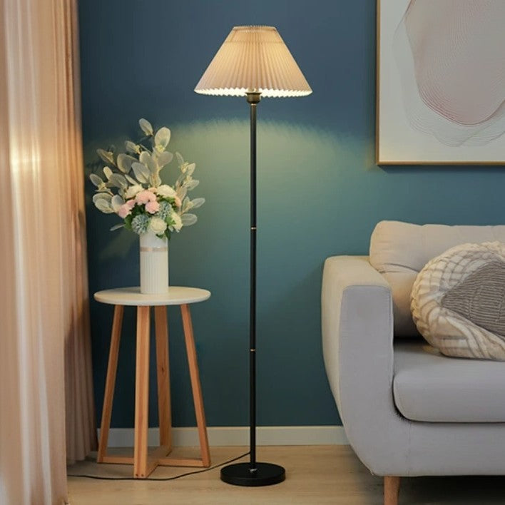 Golvlampa med veckad lampskärm bredvid soffa